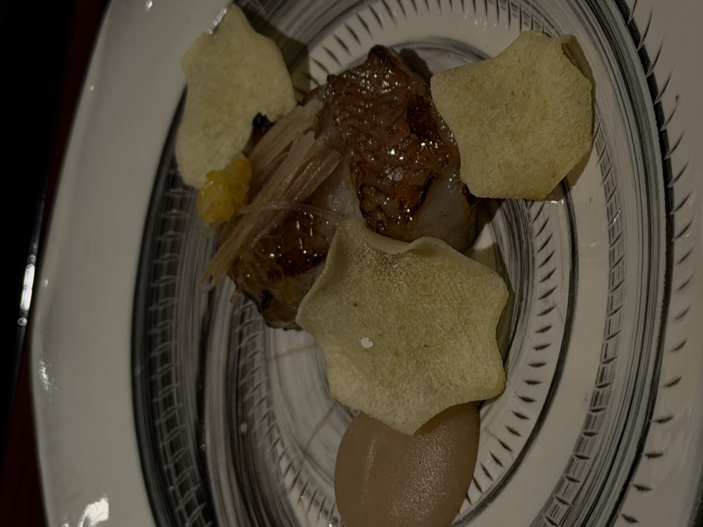 A grilled fillet of thornyhead rockfish with myoga and yuzu zest on a striped plate, with blossom-cut rice crackers and a quenelle of brown purée