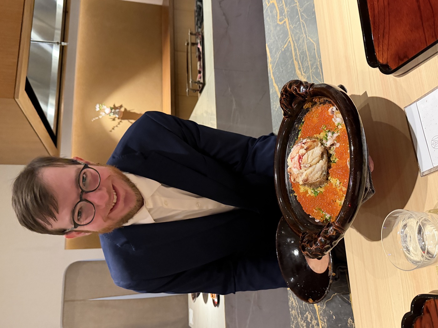 A guest holding up a clay donabe pot brimming with orange salmon roe, crab and rice