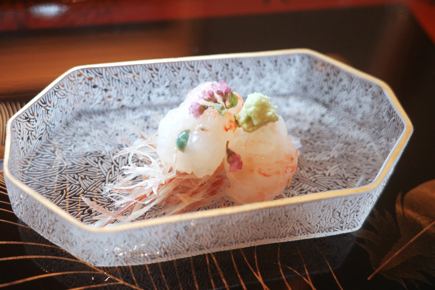 Close-up of the translucent shrimp sashimi with a flower garnish and wasabi