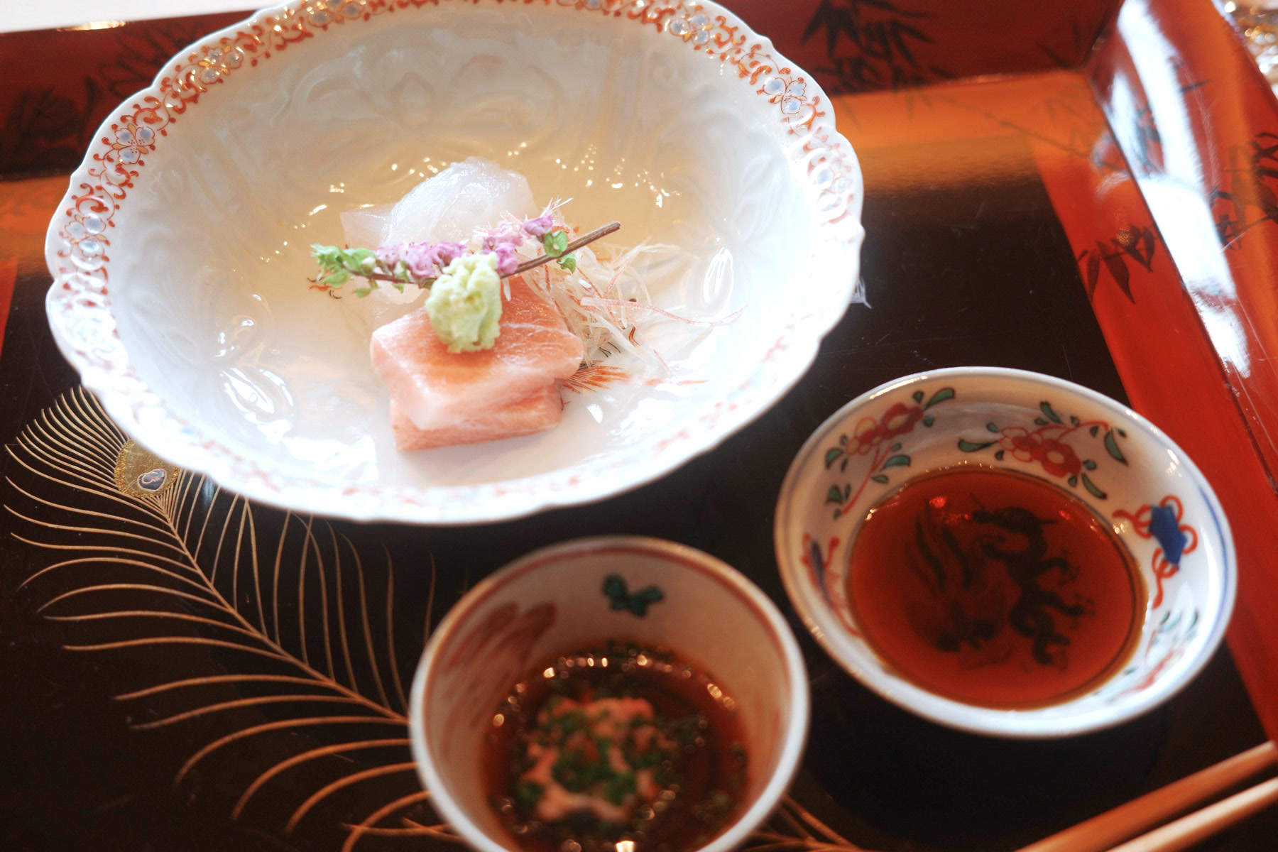 Sashimi in a frilled white bowl with two dipping sauces in small painted cups