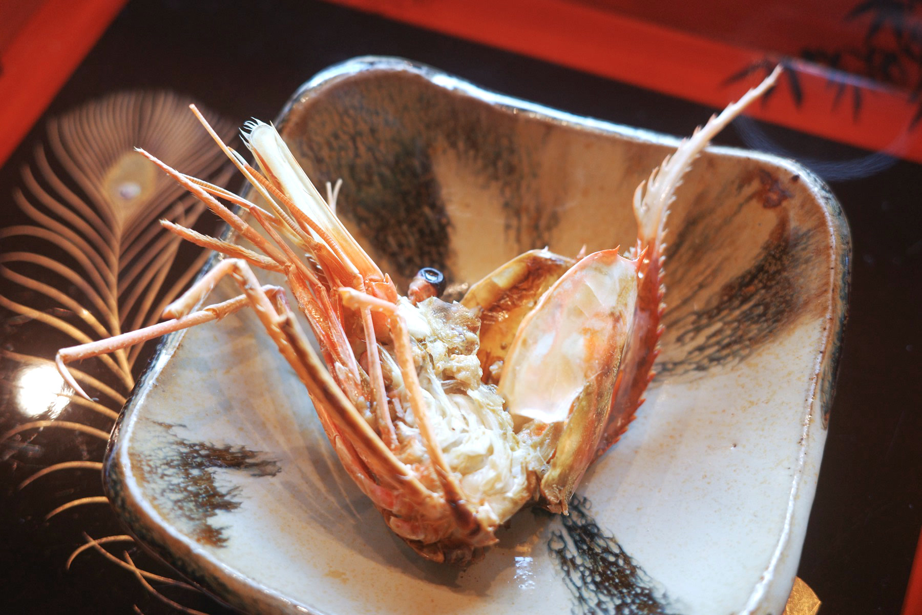 A grilled shrimp head, split open, served in a rustic stoneware dish