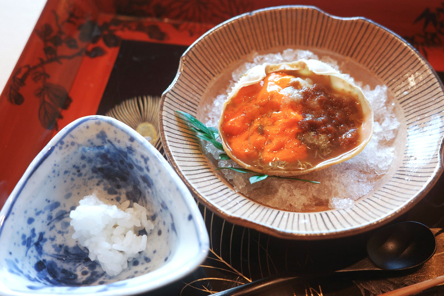 Marinated female snow crab served in its shell on ice, beside a small bowl of white rice