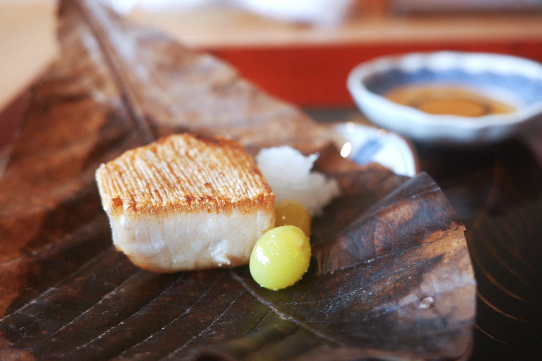 Close-up of the seared edge of the grilled yellowtail beside a single ginkgo nut