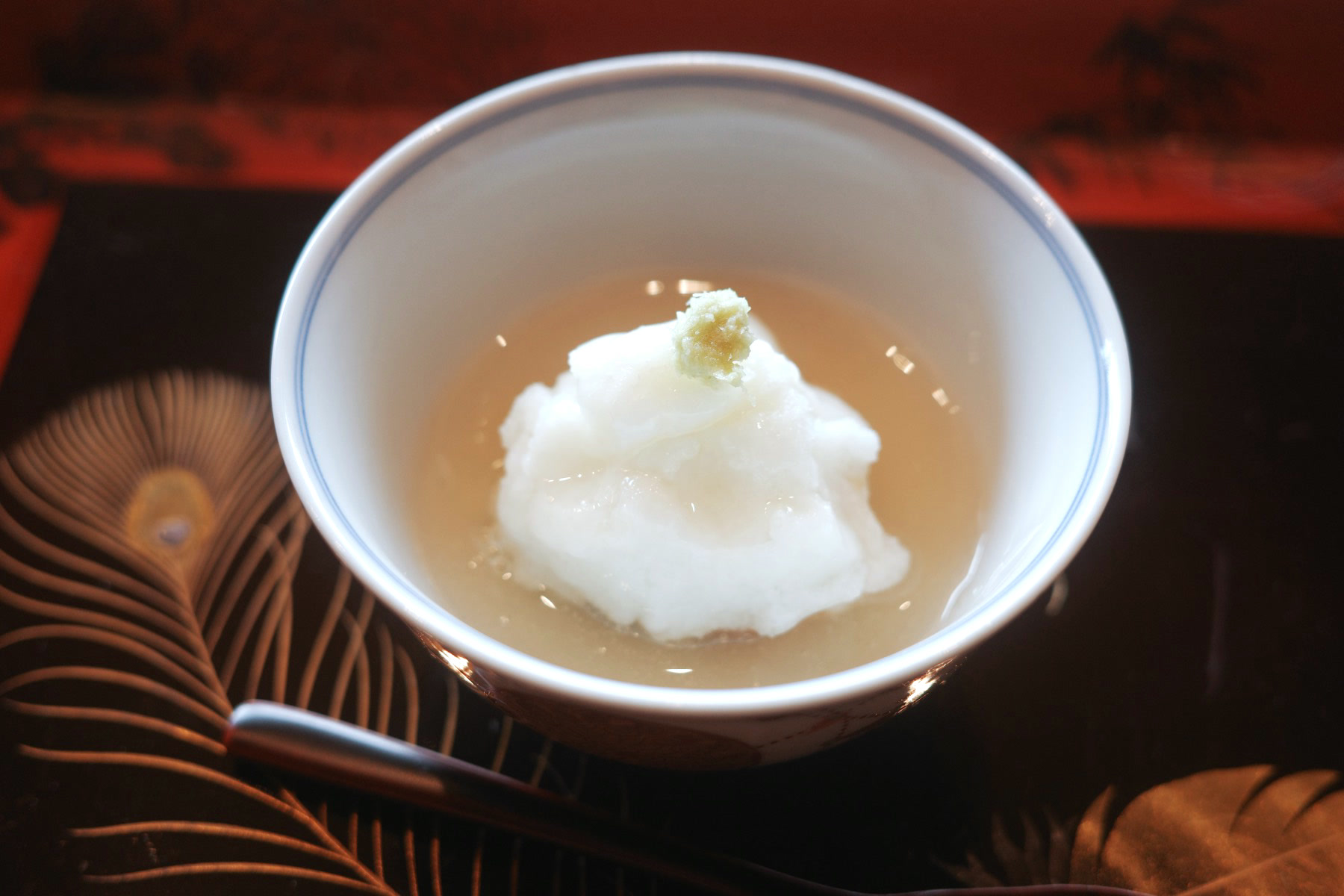 A white bowl of grated steamed turnip over fish in a clear dashi, finished with wasabi