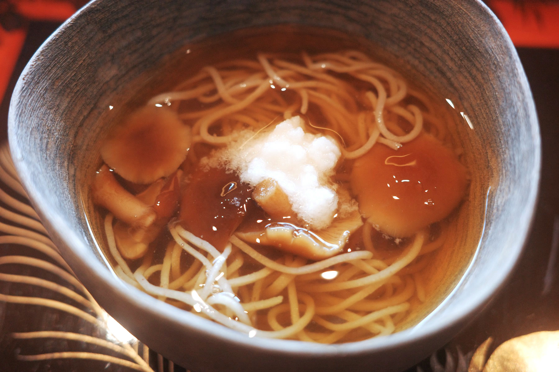Handmade soba noodles in a clear broth with mushrooms and grated daikon, in a grey bowl