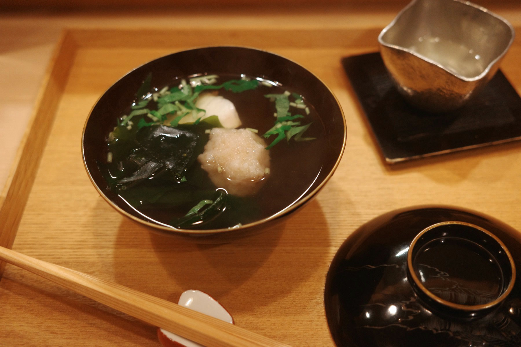 A lacquer bowl of clear soup with a white dumpling, grated daikon, wakame and shiso