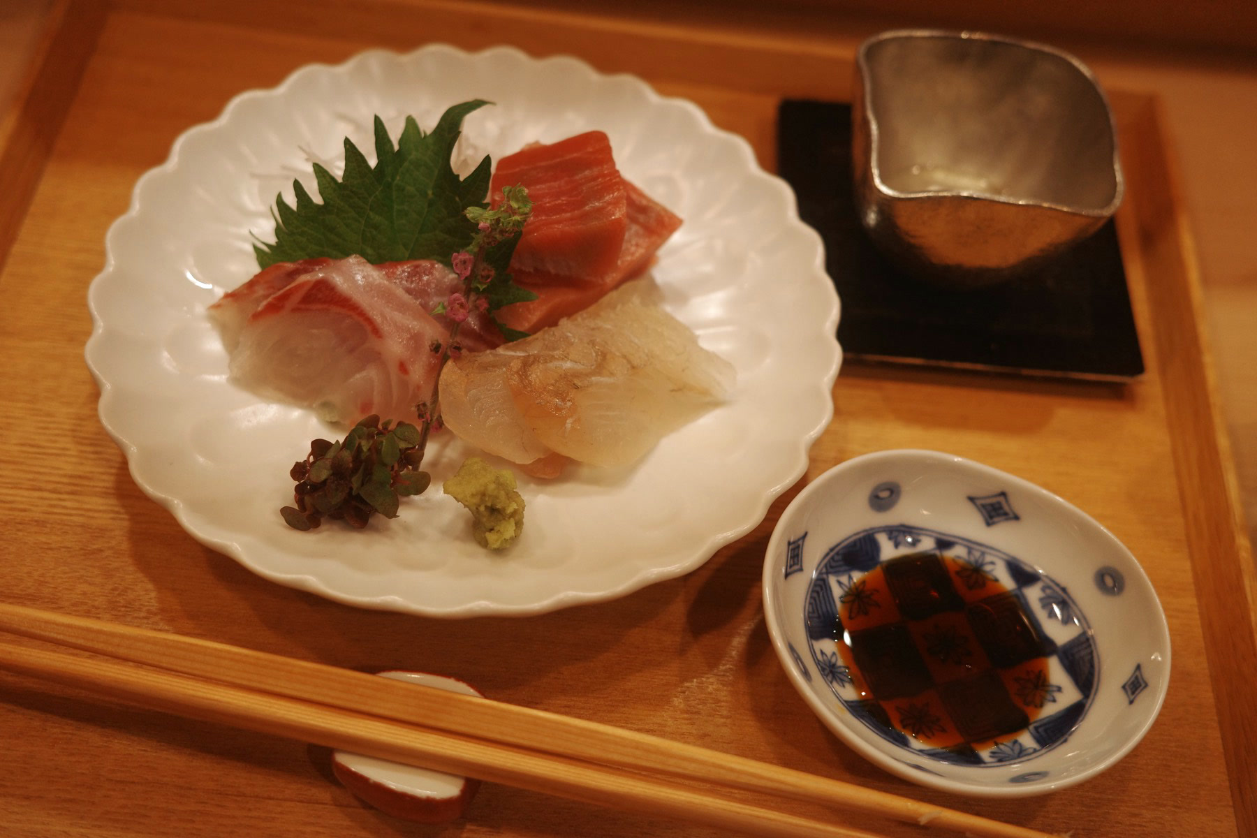 A plate of sashimi — fatty tuna, white fish and a red-skinned fish — with wasabi and a checker-painted dish of soy