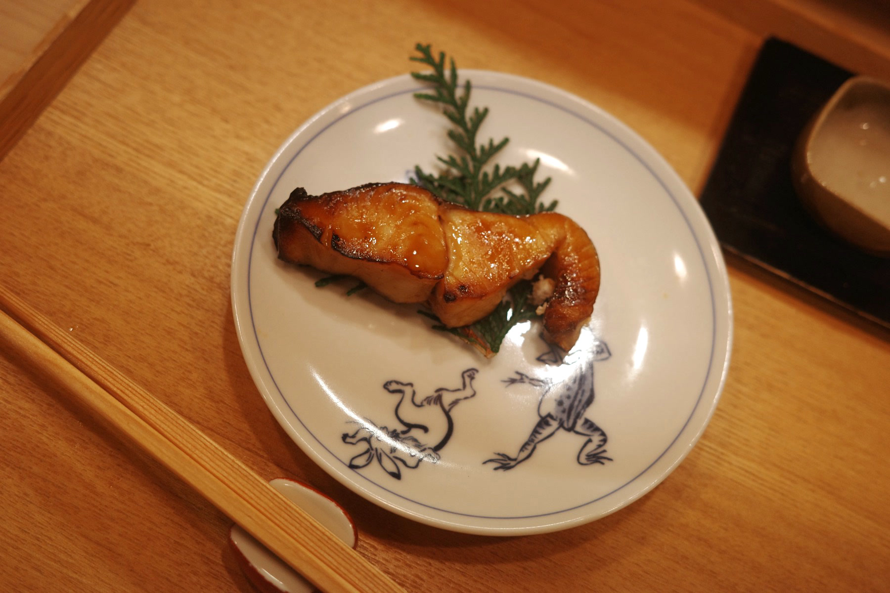 The glazed grilled fish with a sprig of cedar on a blue-rimmed plate