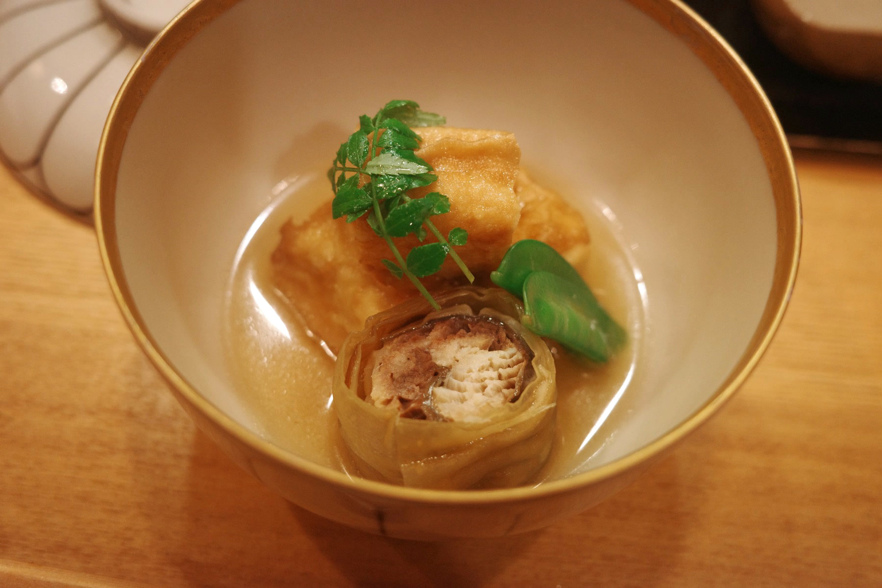 A simmered bowl with fried tofu, a yuba-wrapped roll, snap pea and kinome