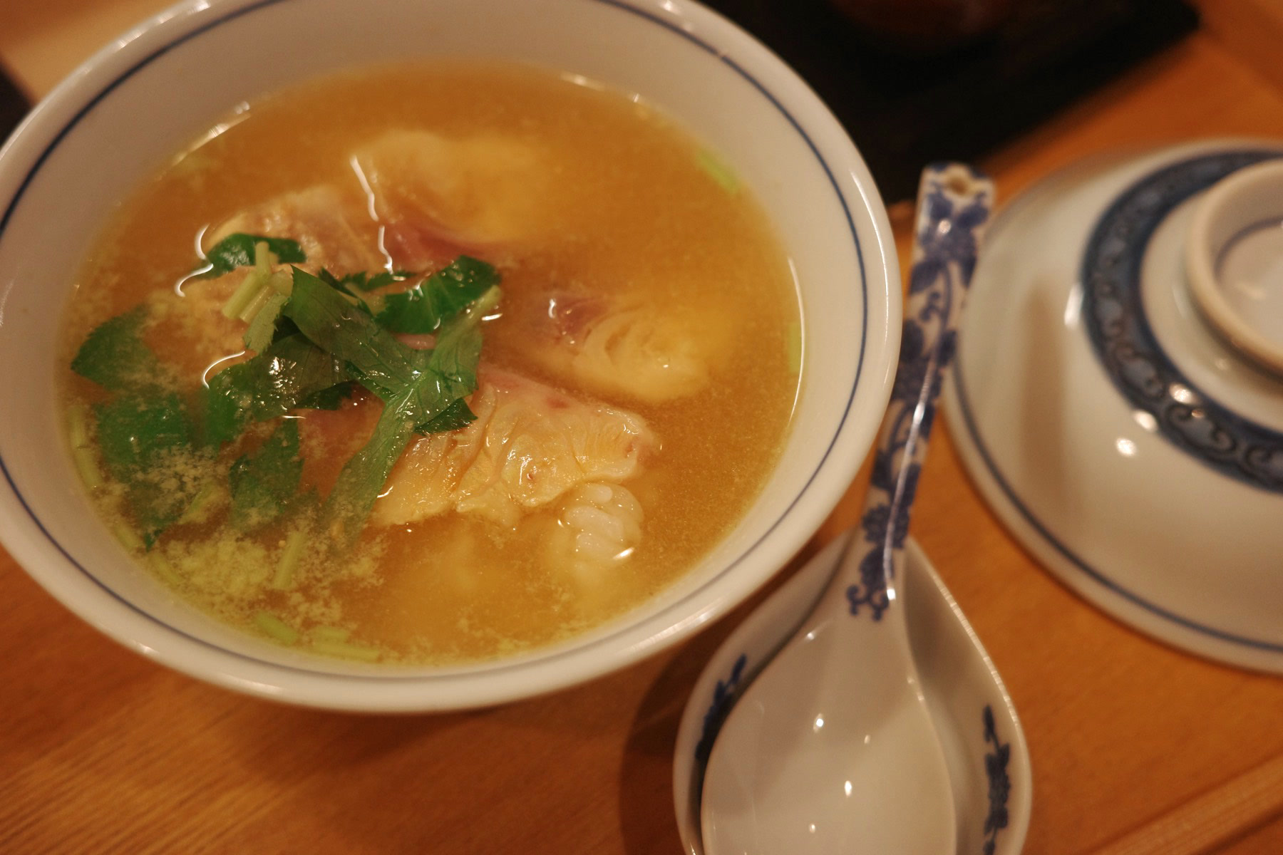 Shrimp wontons in a clear golden broth with mitsuba, with a porcelain spoon