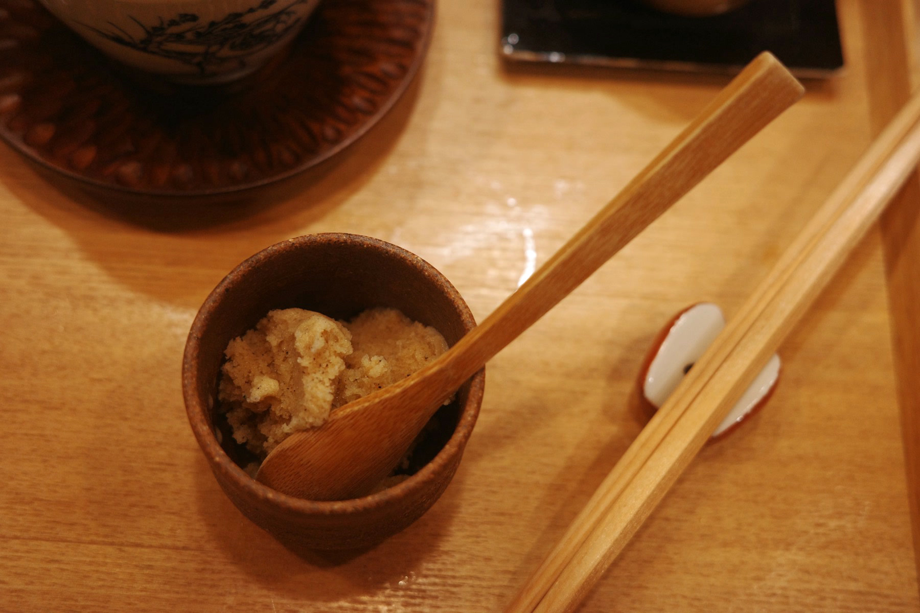 A small wooden cup of a frozen, granular dessert with a wooden spoon